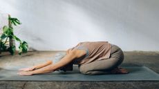 woman grey hair wearing dusky pink vest beige leggings in child pose on grey mat 