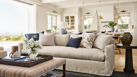 a coastal-inspired living room with a large beige couch, several throw pillows, a plaid coffee table, decor on top, and a side table with a vase on top