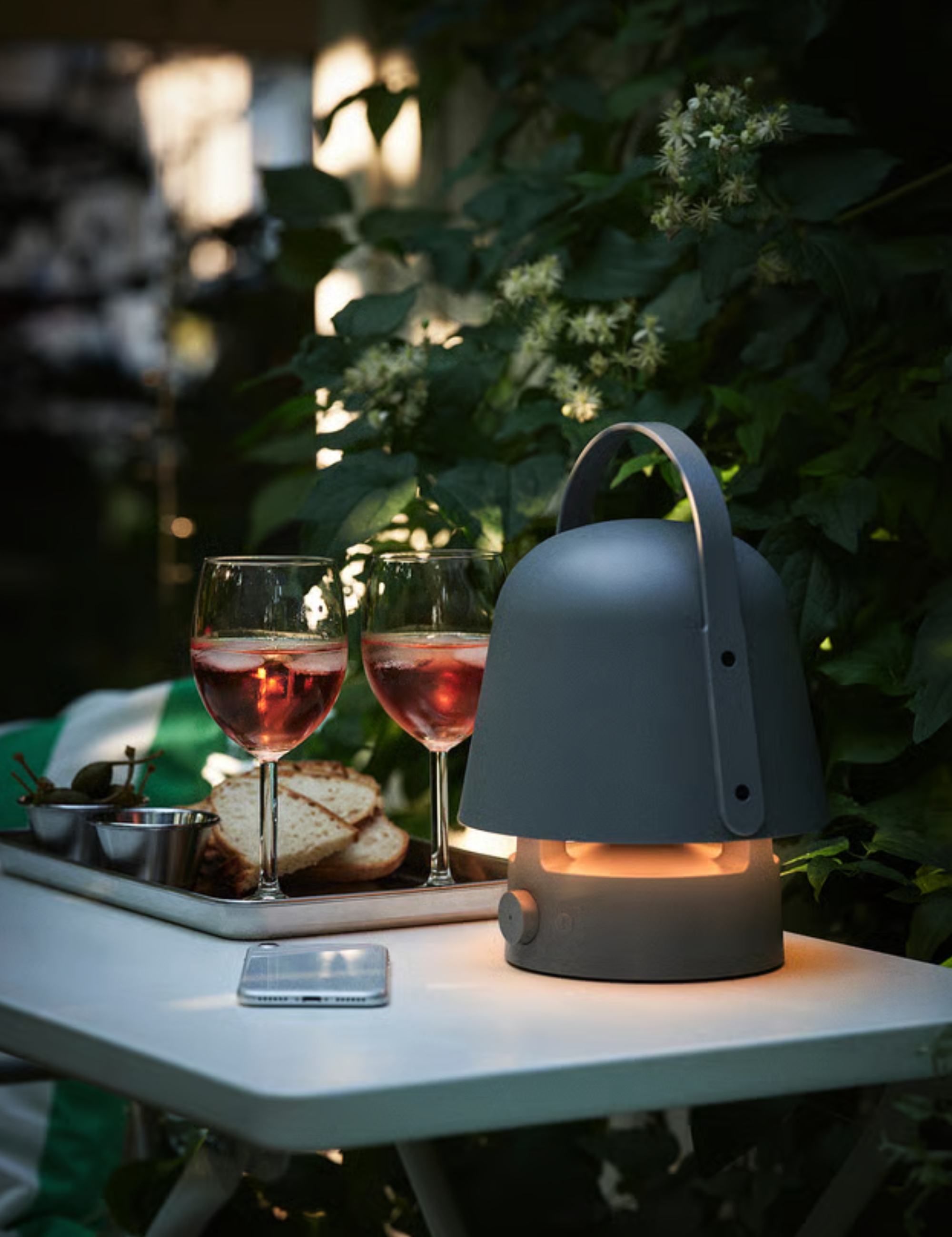 IKEA bluetooth outdoor lamp styled in a leafy patio atop of an outdoor table with shared bites and two wine glasses