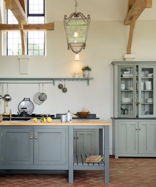 farmhouse kitchen with gray cabinets and terracotta tiled flooring, large exposed wooden ceiling beams