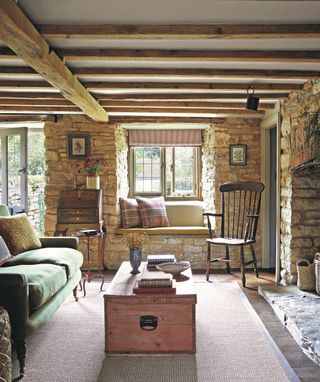 living room with exposed stone walls and beams and green sofa, window seat with plaid cushions and blanket box coffee table