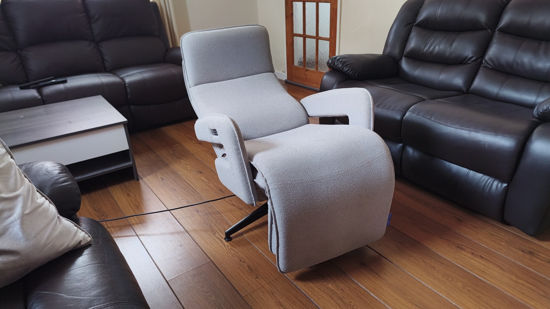 Side view of the recliner fully reclined into its flat position, with its black swivel base visible on the wooden floor.