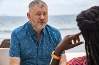 Joe (John Gordon Sinclair) sits on the beach opposite Naomi (Shantol Jackson) who has her back to the camera and is leaning her head on her hand
