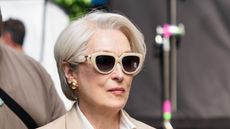 Meryl Streep in The Devil Wears Prada 2, filming wearing a beige coat, navy trousers, striped shirt and red heels