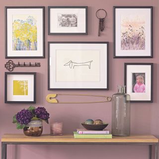 Collection of prints and family photos and quirky items on wall of modern bohemian living room in purple and olive green