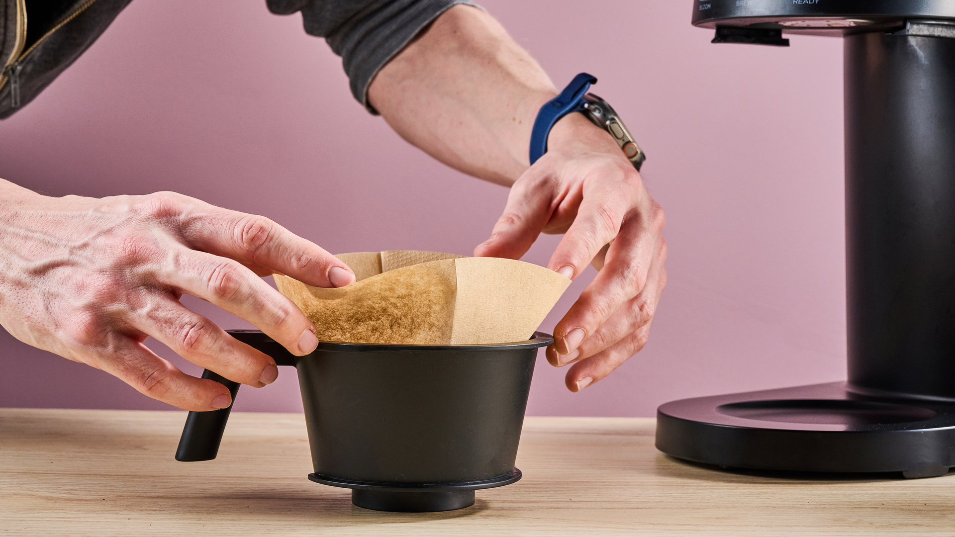 A man folds over the edges of a coffee filter into the Ratio Four's filter basket.