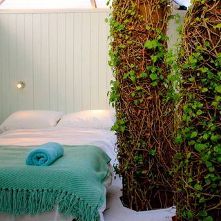 White double bed with green throw and tree trunks inside bedroom
