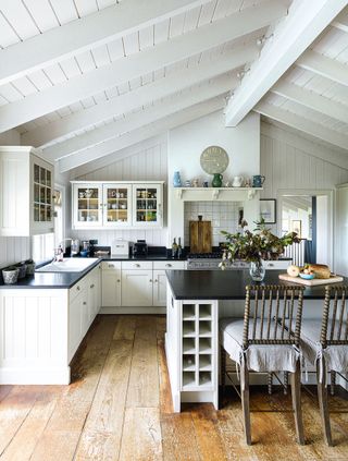 white kitchen with black granite worktops and wooden floors and white clapboard walls and vaulted ceiling