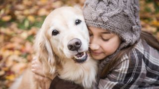 Girl hugging dog in autumn leaves