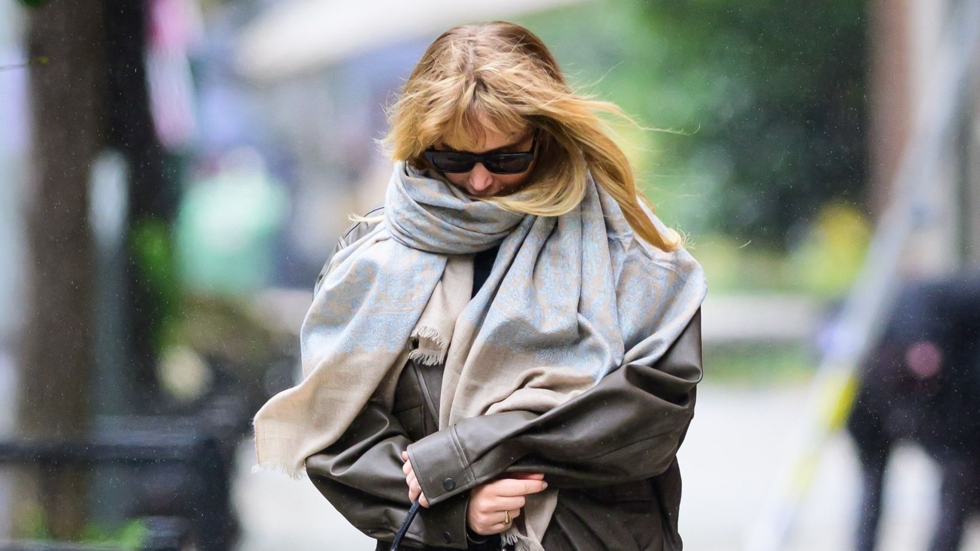 Jennifer Lawrence walks down the street wearing jeans, rounded-toe boots, a leather jacket, a large grey scarf and a black Hermes bag.