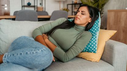 Feeling sick after a sex: A woman lying on the sofa clutching her stomach