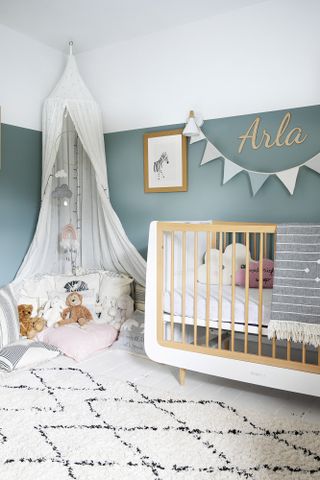 Nursery with blue painted walls, monochrome rug, white and oak cot and white canopy