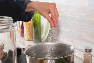 Hand sprinkling salt into a pan of water on the hob