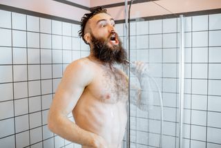 A man opens his mouth in shock while taking a cold shower