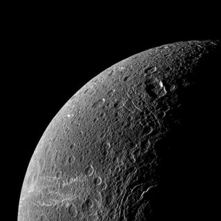 A portion of Dione shows cratered gray surface and white whispy lines across the lower left potion of the image.