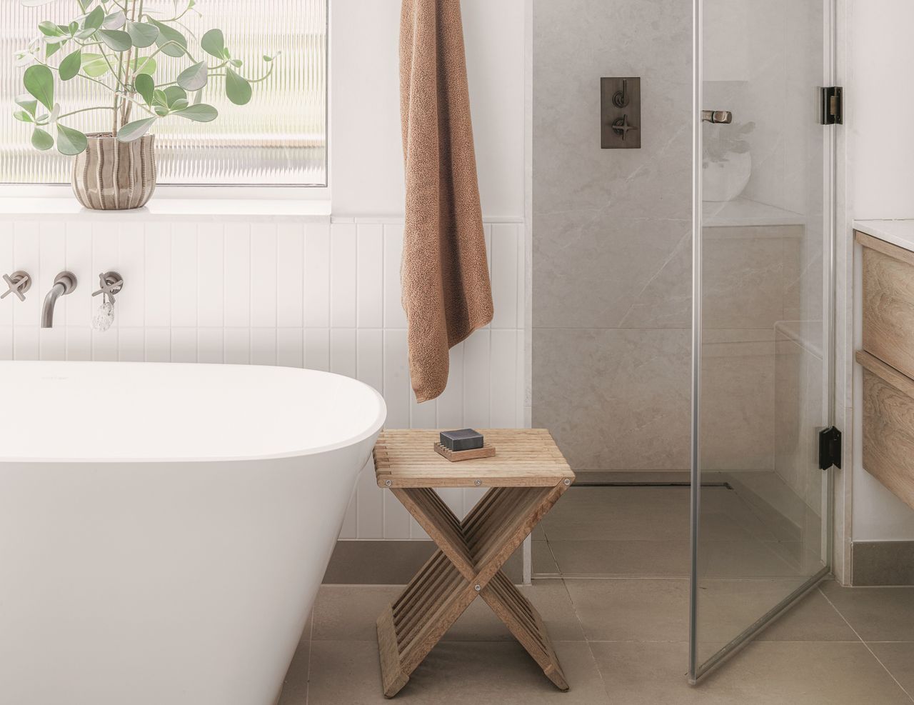 A spa bathroom with a shower, a large white bath, a wooden stool holding soap