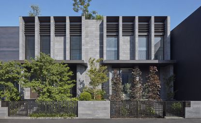 The exterior of a residential home over 2 flows built with grey shades of on create. Low level grey concrete fence with walls and a small front garden with trees