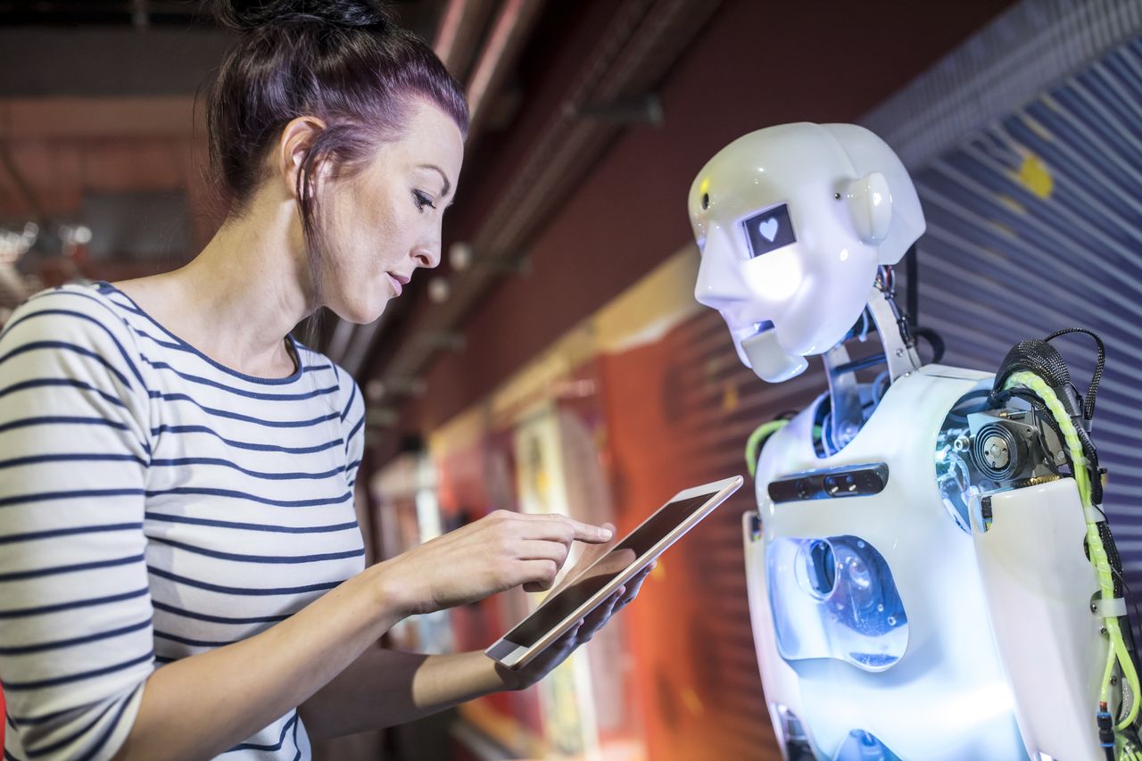 Technician programming humanoid robot using a tablet in a workshop