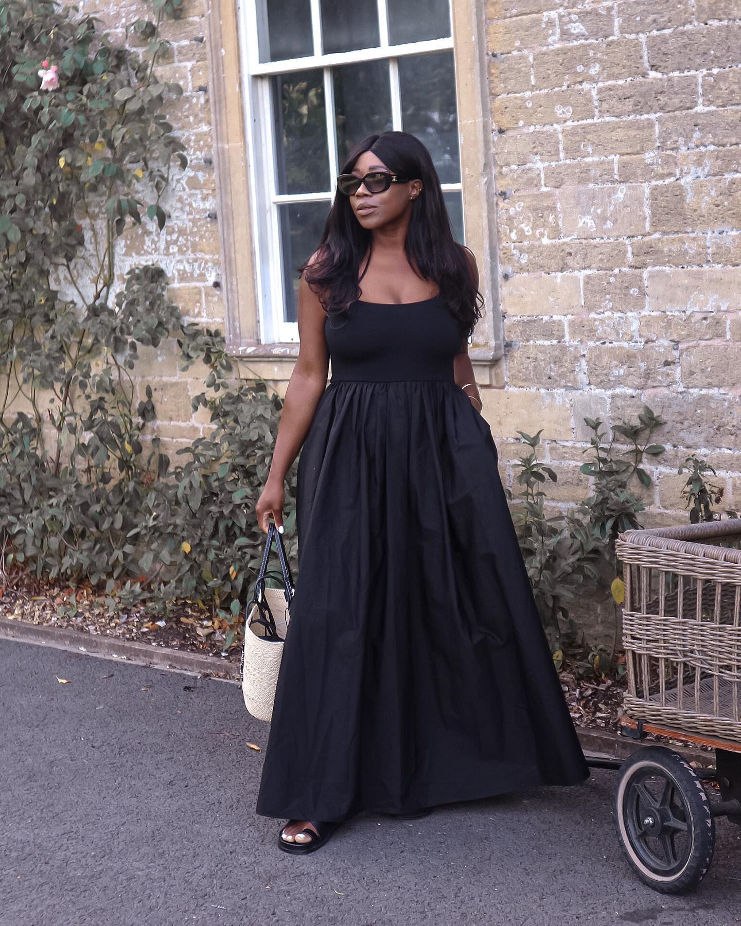 Woman wears black dress, sandals and basket bag