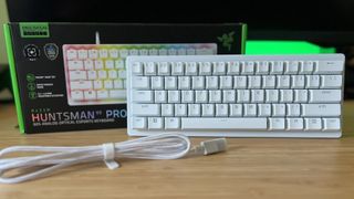 Razer Huntsman V3 Pro Mini gaming keyboard with cable and packaging on a wooden desk