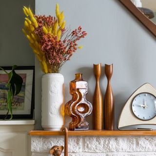 Wooden mantelpiece with orange, wooden decorative items and white vase with orange flowers