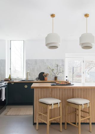 A two-tone kitchen with a wooden panelled kitchen island and two bar stools. Two light pendants hang above the kitchen island.