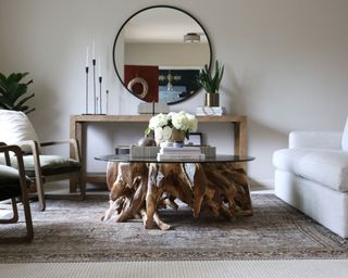 Modern rustic living room with tree root and glass statement coffee table, large round wall mirror & calm neutrals palette