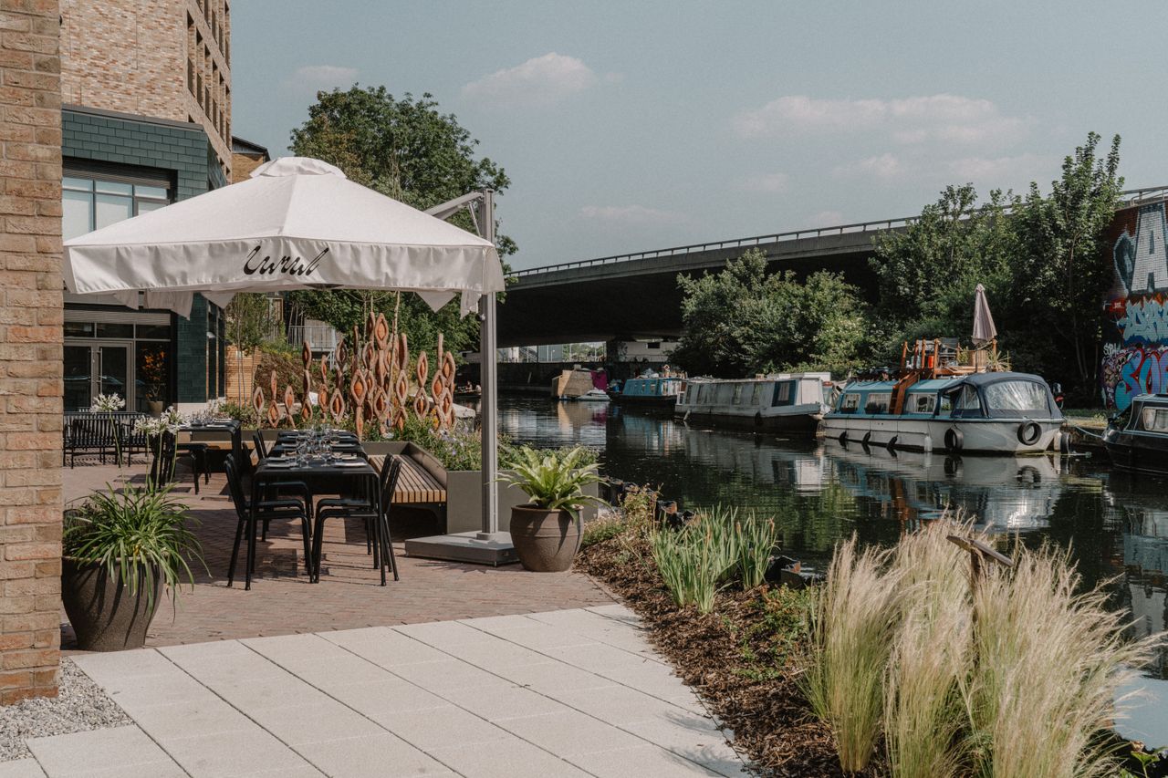 A sun-lit restaurant features brutalist interiors paired with a minimalist, black wrought iron-furnished canal-view terrace.