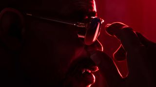 Blade reaching for his glasses in a room filled with red light during the upcoming PC game Marvel's Blade.