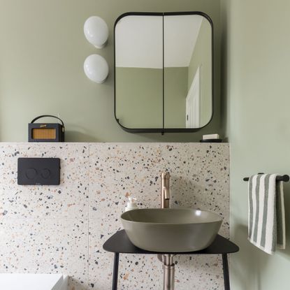 green bathroom with terrazzo tiles and green basin, mirrored cabinet and globe wall lights with a Roberts radio