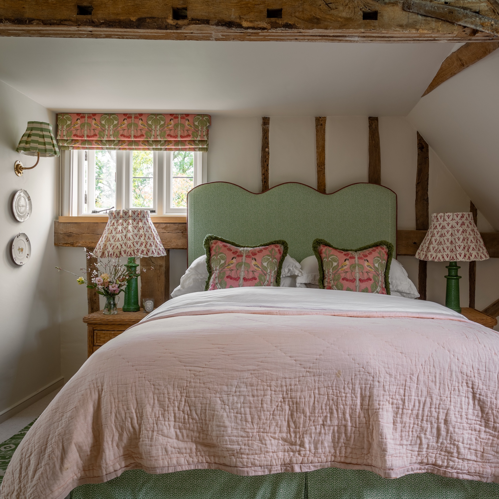 bedroom in English farmhouse with beamed ceiling, pink walls, and bed with green upholstered headboard and pink covers