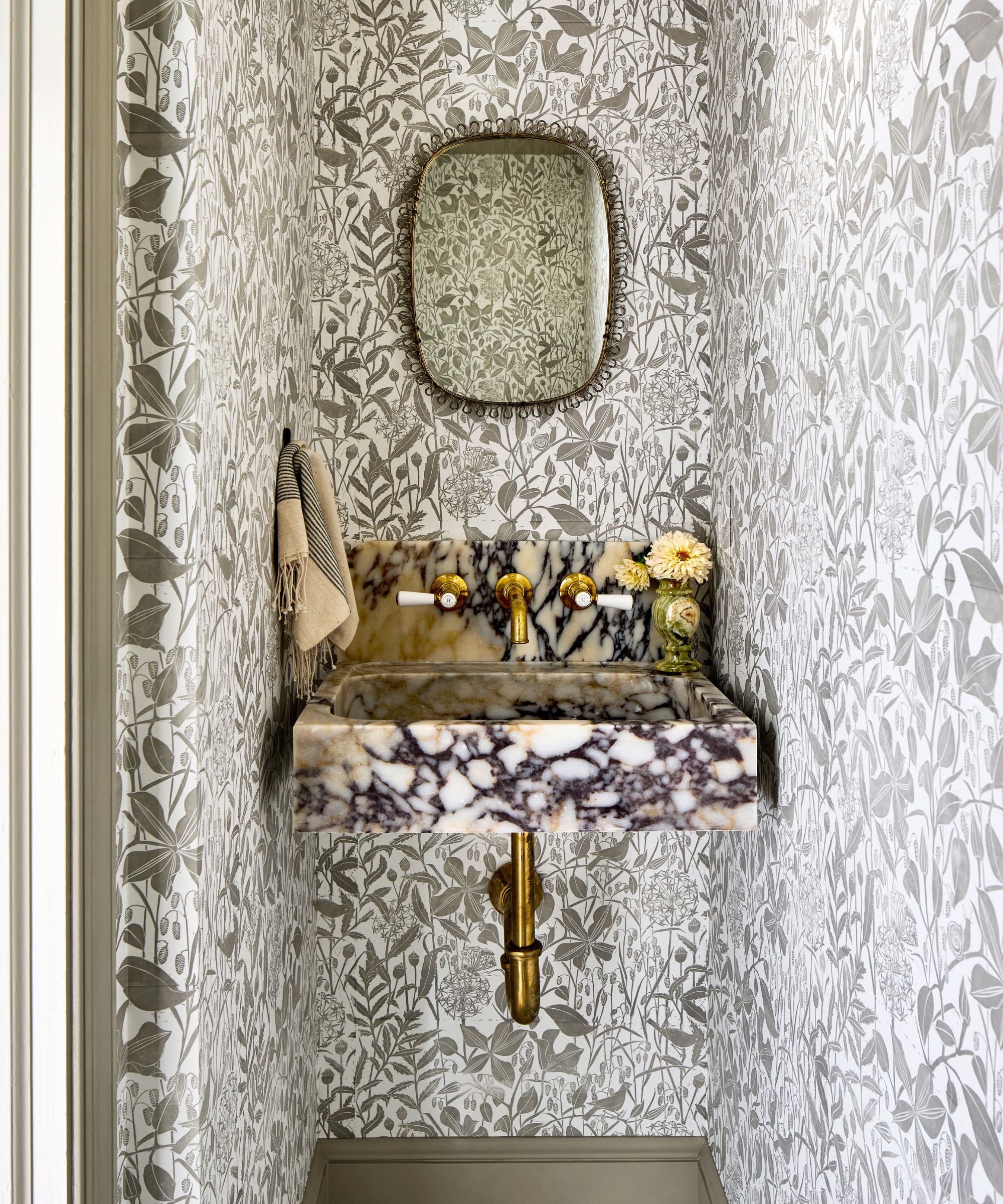 A striking powder room with leafy wallpaper and a marble sink