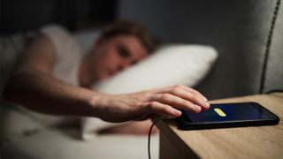 man snoozing his alarm in bed