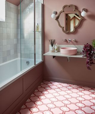 A pink bathroom with pink and red tiles, a sink, shower, and gold mirror
