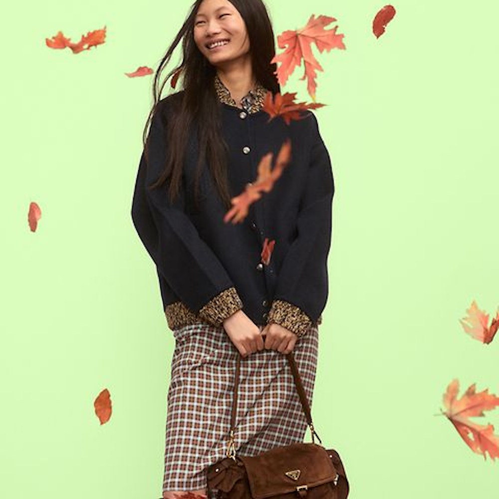 A woman modelling Prada's fall season (available at Farfetch) against a light green background with orange leaves floating in the foreground. 