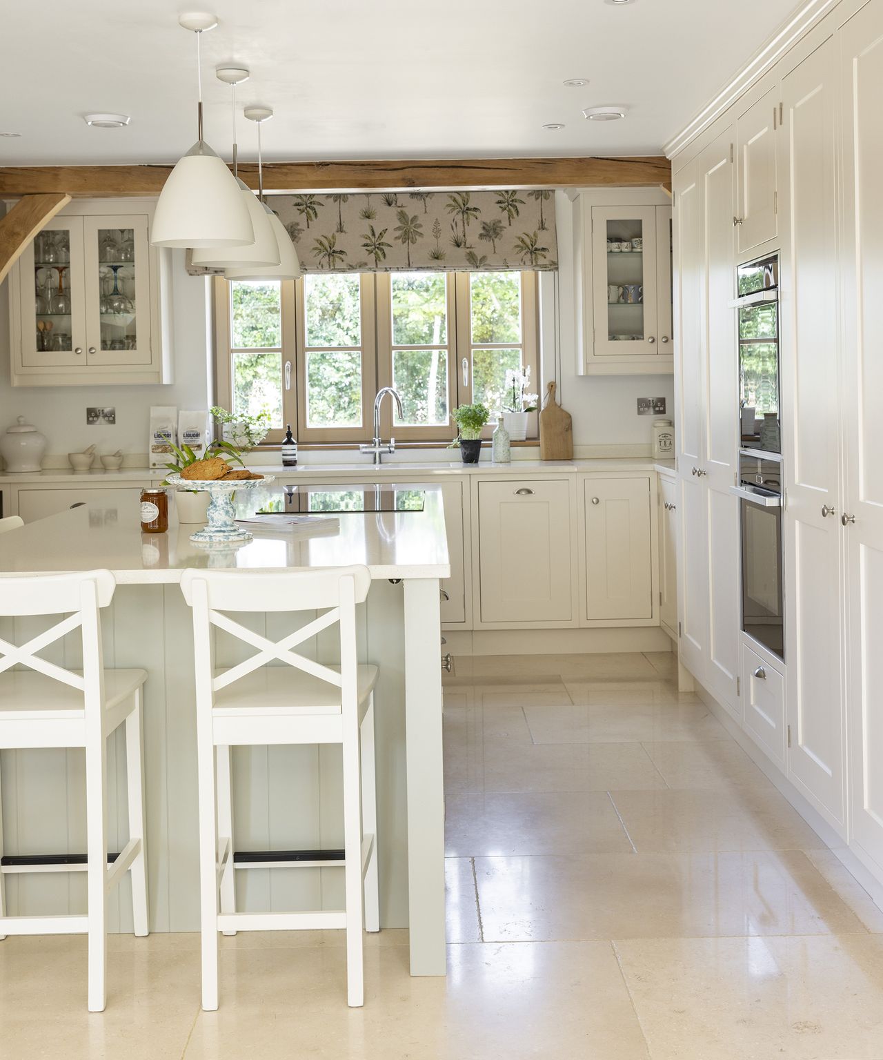 A neutral kitchen with light coloured flooring and cabinetry with central island and exposed beams