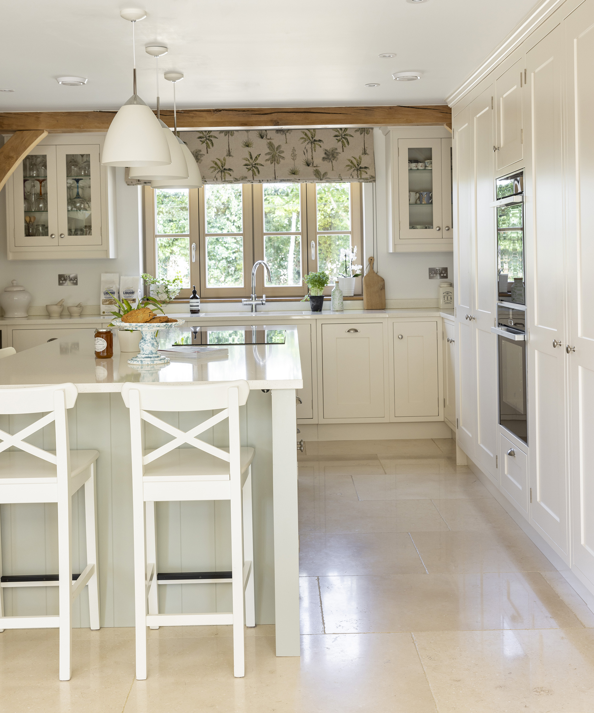 A neutral kitchen with light coloured flooring and cabinetry with central island and exposed beams