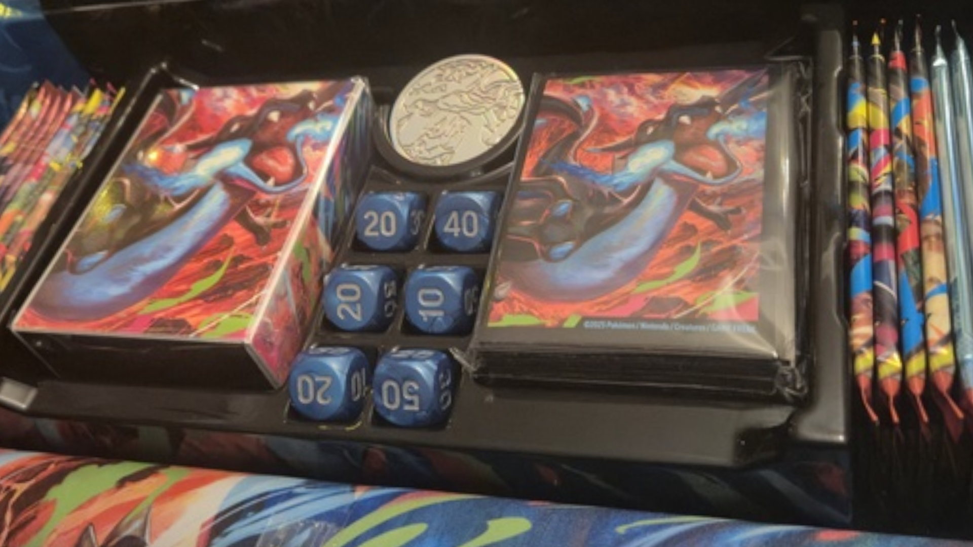 Mega Charizard X booster sleeves, coins, dice, and more in black packaging