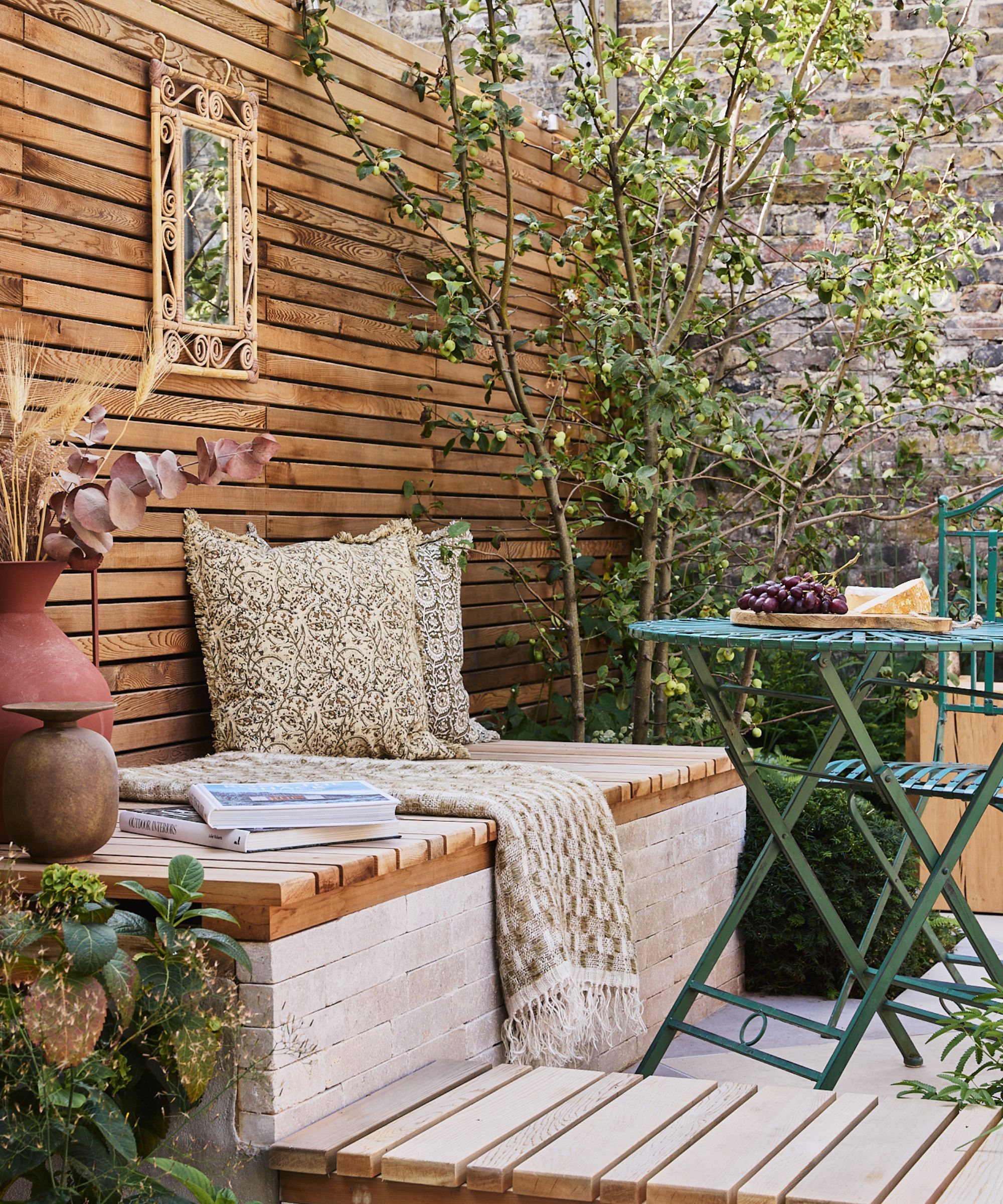 Outdoor terrace with wood clad wall, built-in bench with cushions and a small bistro set