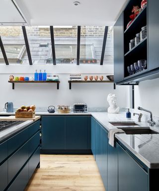 A blue U-shaped kitchen with white walls, open shelving and a skylight.