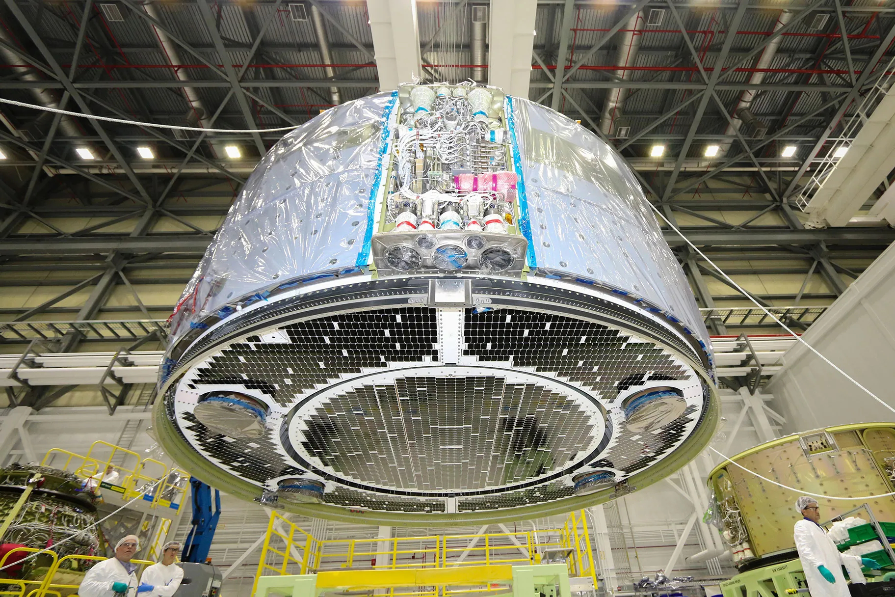 a large cylinder is suspended over a factory floor. It is wrapped in plastic with black tiles lining the bottom.