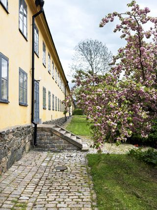 Hotel Skeppsholmen, Stockholm. The side view of a beige double storey building with a stone pathway next to it and a green lawn.