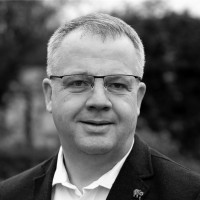 man smiles to camera wearing glasses in a suit