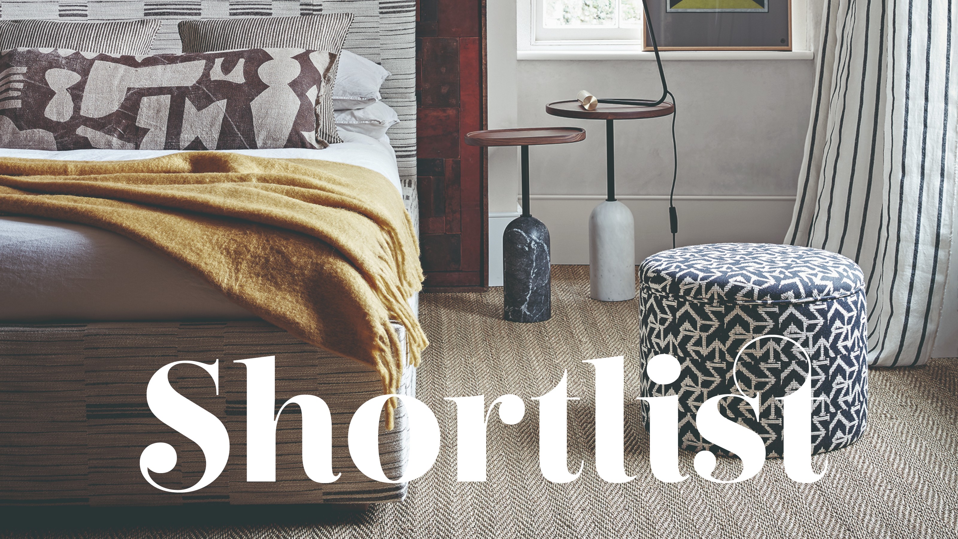 A bedroom with a patterned upholstered bed and a black and white patterned storage stool next to it