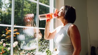 Woman drinking water in workout clothes, representing how dehydration is one of the common causes of constipation