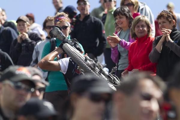A rider, cheered on by many, as he hikes his bike upward.