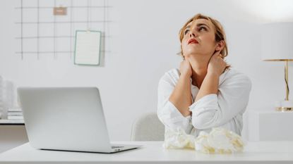 Woman experiencing tech neck pain with an open laptop next to her, wellness tips
