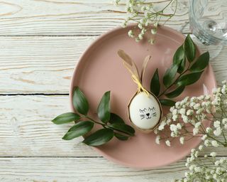 Simple and sweet Easter place setting with pink plate, bunny head egg, and fresh foliage sprigs.