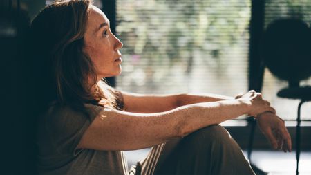Thoughtful mature woman sitting on the floor in the kitchen.