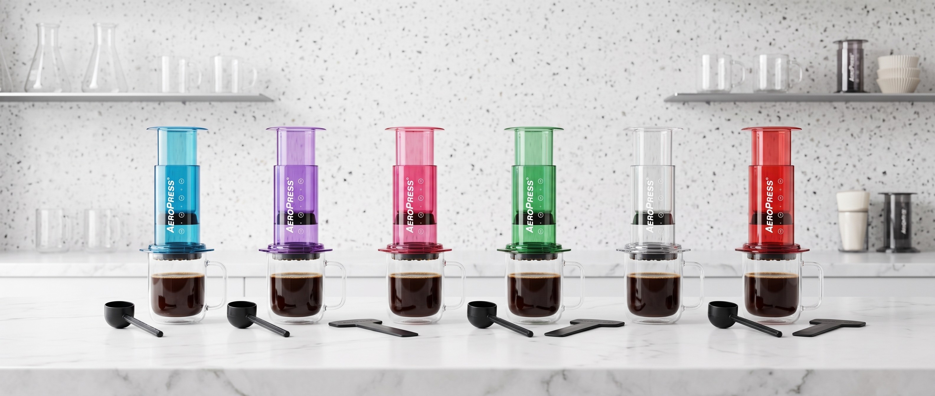 Collection of different colored AeroPress coffee makers lined up on white kitchen counter